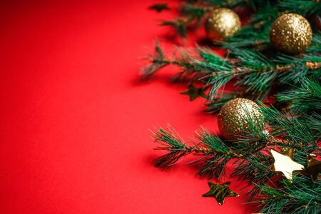 Christmas or Christmas ornaments background: Christmas tree branch and golden glass balls golden stars on a red background with space for textの写真素材