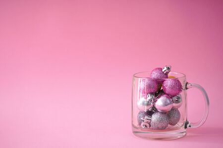 Pink and gray christmas balls in a transparent glass cup, on a pink background, Place for textの写真素材