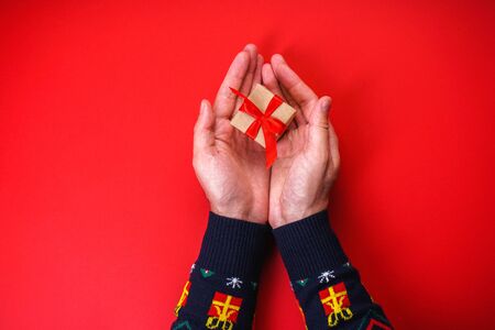 Male hands in a Christmas sweater with a gift on a red background.の写真素材