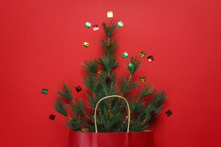 Christmas concept. Green spruce branches in a package of red paper on a red background with...