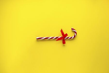 Christmas concept. Christmas candy cane with a red bow on a yellow background. Flat lay.の写真素材