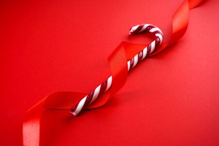 Christmas concept. Christmas candy cane with red ribbon on a red background. Close-up.の写真素材