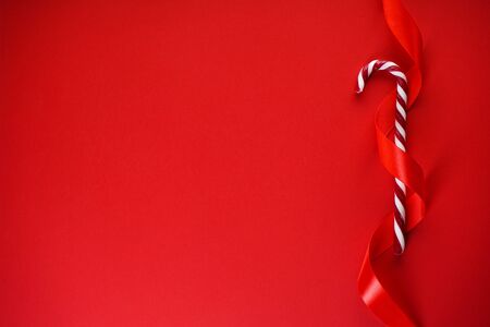 Christmas concept. Christmas candy cane with red ribbon on a red background. Flat lay, place for text.の写真素材