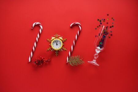 Yellow vintage alarm clock with sweets and a glass with confetti on a red background. Flat lay.の写真素材