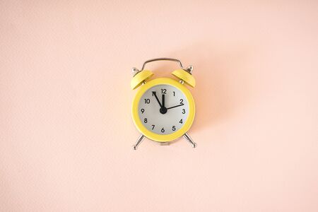 Yellow alarm clock on a beige background. Flat lay.