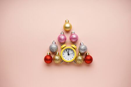 Yellow alarm clock with New Year toys in the form of a tree, on a beige background. Flat lay
