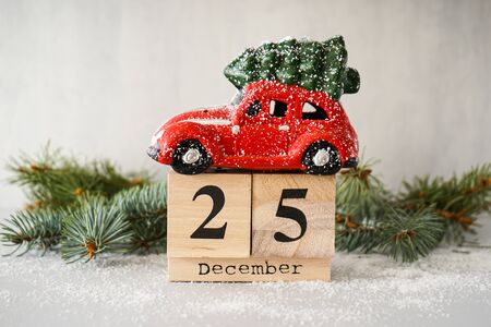 Red Christmas toy car on an old wooden calendar on a gray background with a fir branch. Christmas...