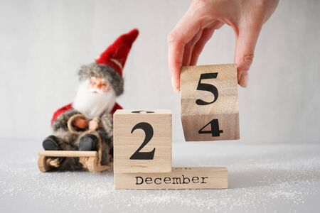 Christmas composition. Snow, toy Santa Claus in a sleigh with an old wooden calendar on a gray...