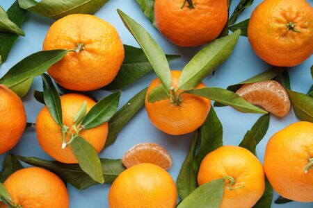 Flat lay. Fresh orange tangerines with green leaves, on a blue background.