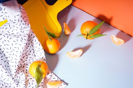 Fresh orange tangerines with leaves with a yellow cutting board and a towel, on a colorful background.の写真素材