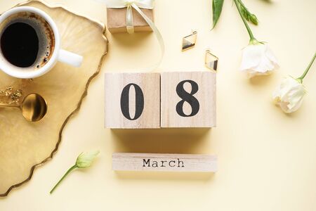 Cup of coffee and a wooden calendar with a gift box, beautiful flowers on a yellow background. Place...