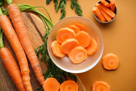 Fresh carrots on a wooden kitchen board and carrots in small slices on a brown background. Flat lay.