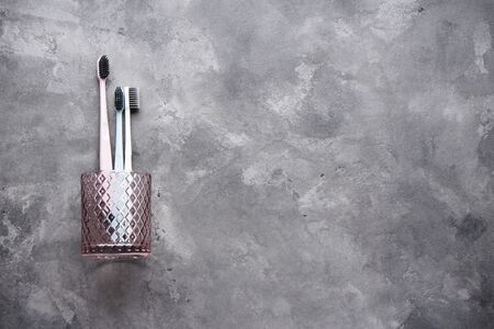 Flat lay composition of multi-colored toothbrushes in a glass cup on a gray background with space for textの写真素材