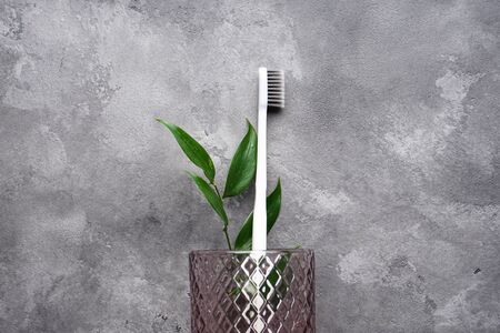Flat lay composition of a white toothbrush in a glass on a gray background. Space for text.の写真素材