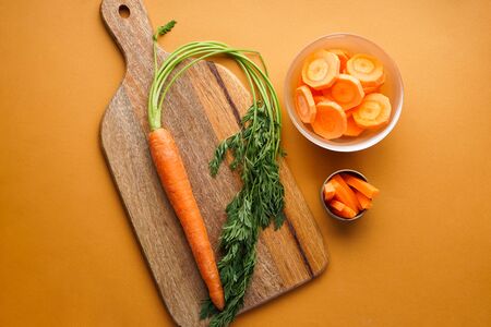 Flat lay composition with ripe fresh and chopped carrot on a brown background.