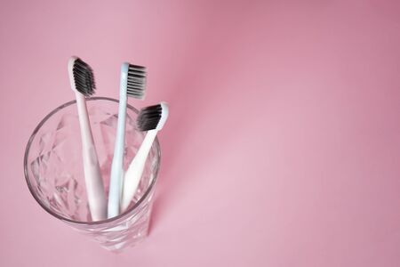 Toothbrushes in a glass on a pink background, flat lay with space for text. Dental and healthcare...