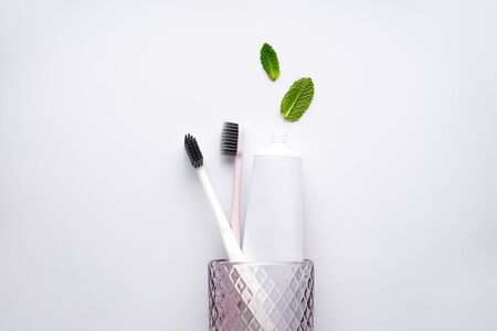 Toothbrushes and toothpaste in a glass on a white background with mint leaves. Flat lay, closeup.の写真素材