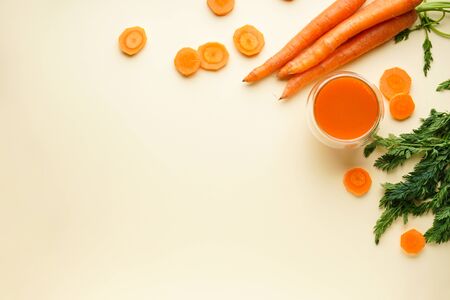 Fresh carrot juice and ripe carrots on a yellow background. Flat lay, space for text.