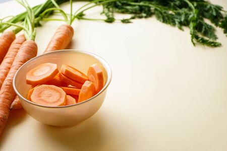 Fresh carrots on a wooden kitchen board and carrots in small slices on a pastel yellow background. Space for textの写真素材