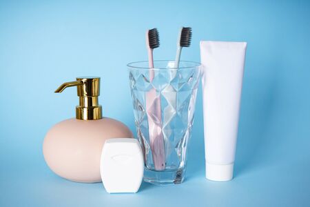 Toothbrushes in a glass, toothpaste and dispenser on a blue background. Dental and morning concept.
