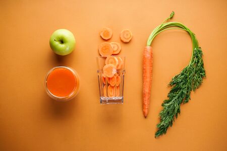 Flat lay. Fresh carrot juice, apple and fresh carrots on a brown backgroundの写真素材
