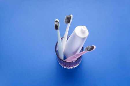 Multi-colored toothbrushes in a glass on a blue background. Flat lay composition.