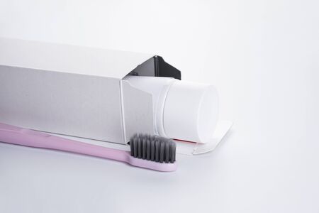 Pink toothbrush with black bristles and toothpaste in a package on a white background. Close-up.