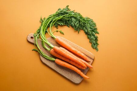 Ripe fresh carrots on a wooden kitchen board with a brown background. Flat lay composition.