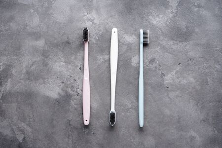 Flat lay composition of multi-colored toothbrushes with black bristles on a gray background.	