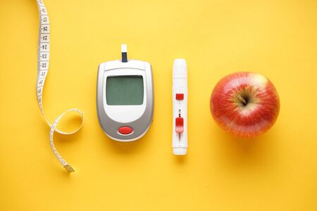Diabetes concept. Digital glucometer, lancet pen, centimeter and fruits on red background close-up. の写真素材