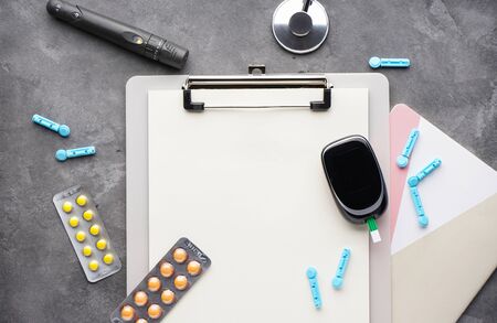 Diabetes concept. Digital glucometer, lancet pen, tablets and stethoscope on gray background with space for text, flat lay.の写真素材