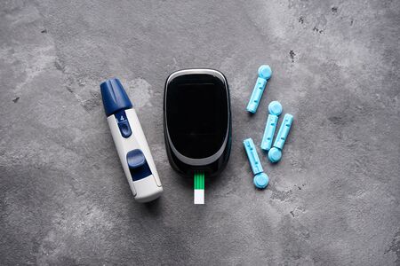 Diabetes concept. Blood glucose meter. Digital glucometer and lancet pen on gray background, close-up.の写真素材
