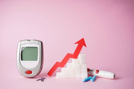 Diabetes concept. Digital glucometer, lancet pen and sugar on a pink background.の写真素材