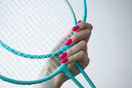 Beautiful manicure. Beauty and sport concept. Beautiful female hand holds a badminton racket on a white background.の写真素材
