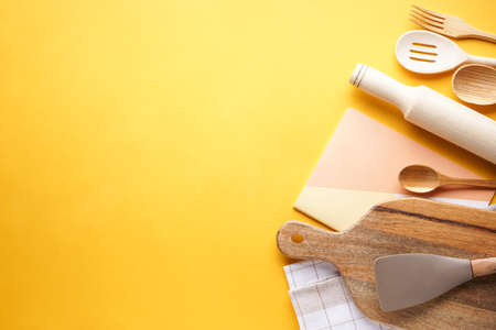 Wooden kitchen utensils with a towel on a yellow background with space for text, top view.