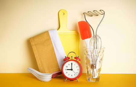 Various kitchen utensils in a glass and clock on a yellow background with space for text.の写真素材
