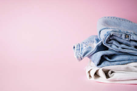 Folded different jeans on a pink background, place for text.の写真素材