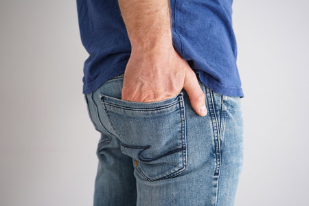 Legs of a young man in jeans with a hand in a pocket on gray background.