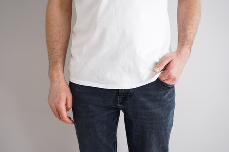 Legs of a young man in jeans with a hand in a pocket on gray background.