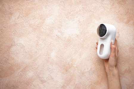 Female hand with modern fabric shaver on color background, place for text. Top view.