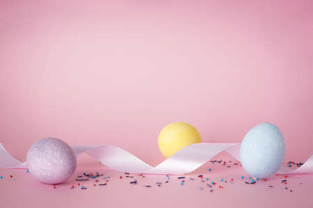 Easter eggs and white ribbon on a pink background, place for text. Happy Easter concept.の写真素材