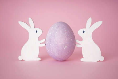 Easter wooden bunnies with Easter egg on a pink background. Happy Easter concept.