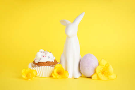 Easter bunny and delicious easter cupcake on yellow background.