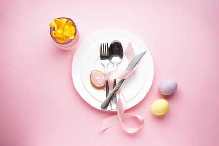 Easter holiday concept. Easter holiday table setting on a pink background. Plates with colorful...
