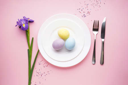 Easter table with daffodil and cutlery on a pink background, flat lay, space for text.