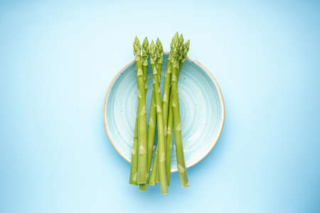 Green asparagus in a plate on a blue background, top viewの写真素材