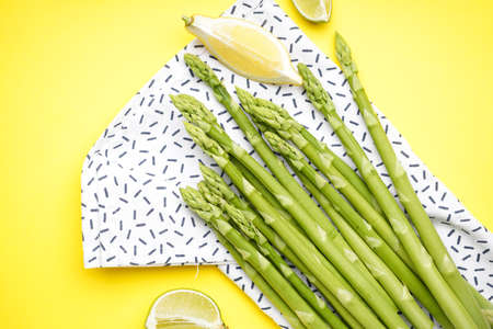Green asparagus with lemon and tea towel on yellow background. Close-upの写真素材