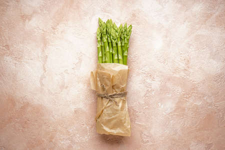 Fresh green asparagus in paper on beige background, flat layの写真素材