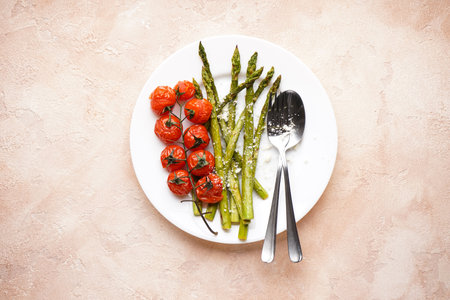 Baked asparagus and cherry tomatoes in a plate on a beige background. Top view.の写真素材