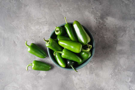 Green jalapeno peppers in a plate on a gray background, top view.